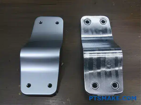 Comparison of metal automotive brackets showing Dacromet coating versus galvanized finish on workshop surface