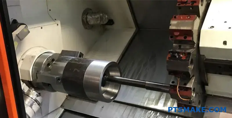 A close-up view of a CNC lathe machine turning a long steel shaft, with the chuck holding the workpiece and the turret with cutting tools visible.